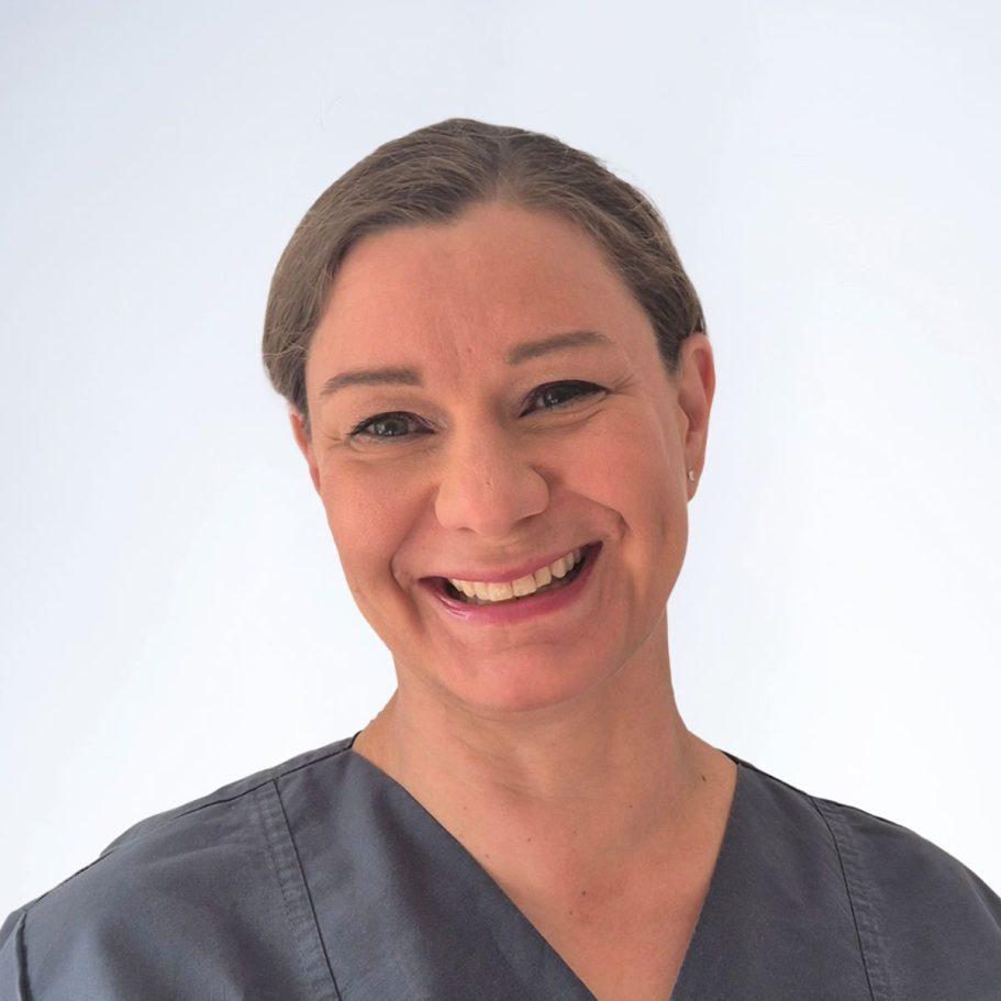Dr. med. dent. Silke Pietzka. Lächelnde Frau in blauer medizinischer Kleidung vor hellem Hintergrund.