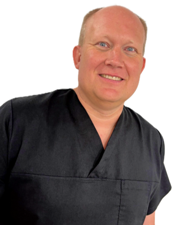 Portrait Dr.met. Dr.met dent. Sebastian Pietzka. Lächelnder Mann in medizinischer Kleidung mit kurzen Haaren und hellem Hintergrund.