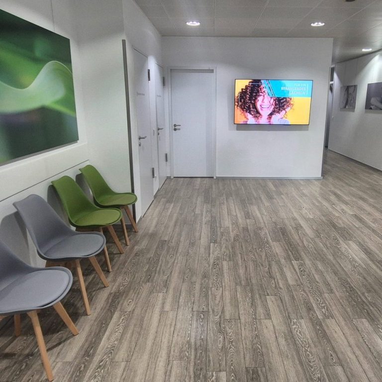 Helle Empfangshalle mit Stühlen, einem TV-Bildschirm und modernen Wandbildern.