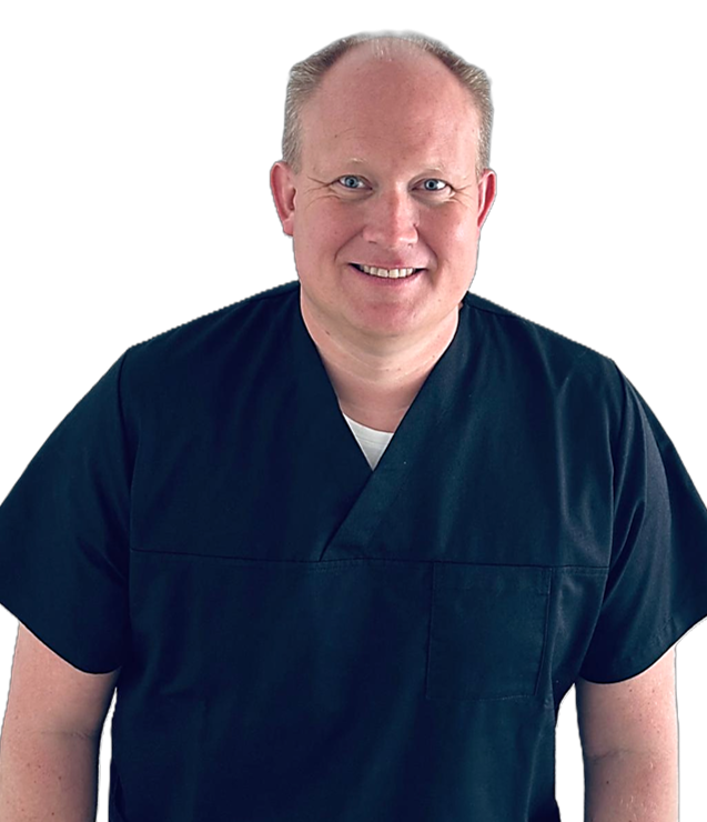 Portrait Dr.met. Dr.met dent. Sebastian Pietzka. Lächelnder Mann in medizinischer Kleidung mit kurzen Haaren und hellem Hintergrund.